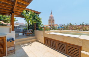 A rooftop terrace with a pool, outdoor seating, and a view of a historic tower.