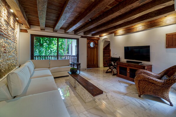 A living room with a sofa, a wooden bench, a wicker chair, a television, and a stone wall.