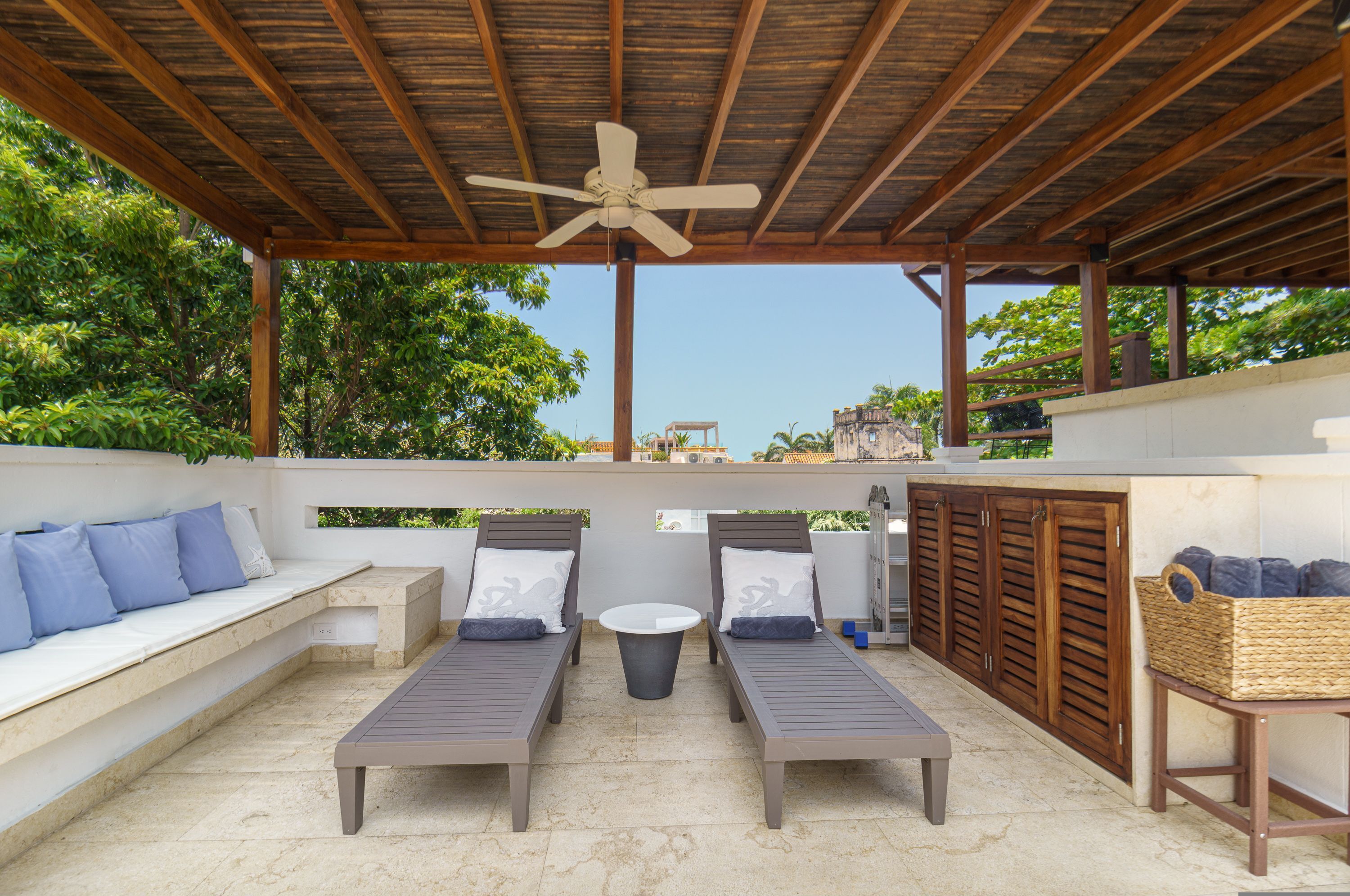 A covered outdoor seating area with two lounge chairs, a small round table, and a ceiling fan.