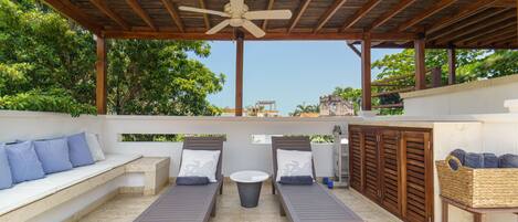 A covered outdoor seating area with two lounge chairs, a small round table, and a ceiling fan.