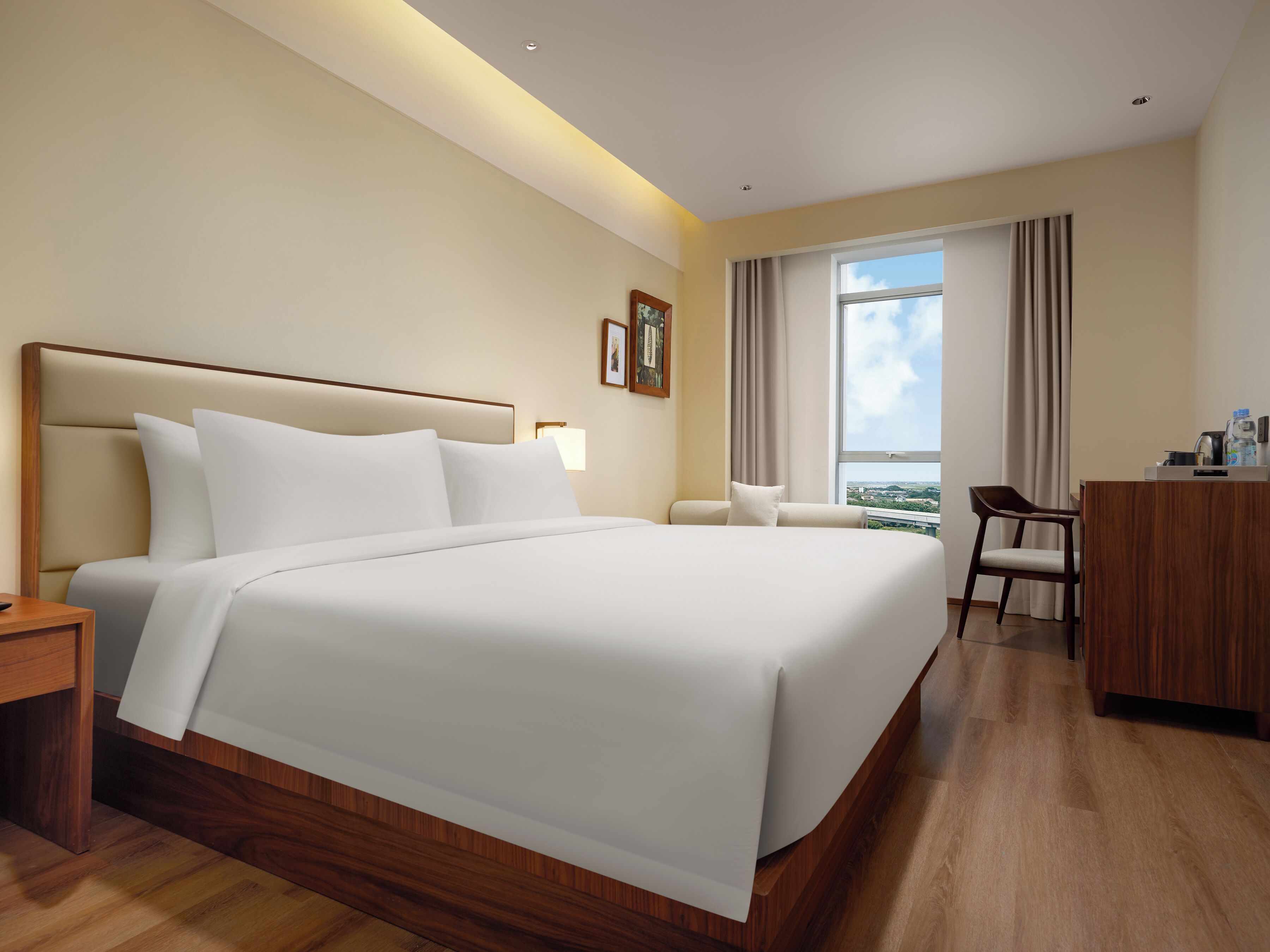 A hotel room with a large bed, a desk, a chair, and a view of the city through the window.
