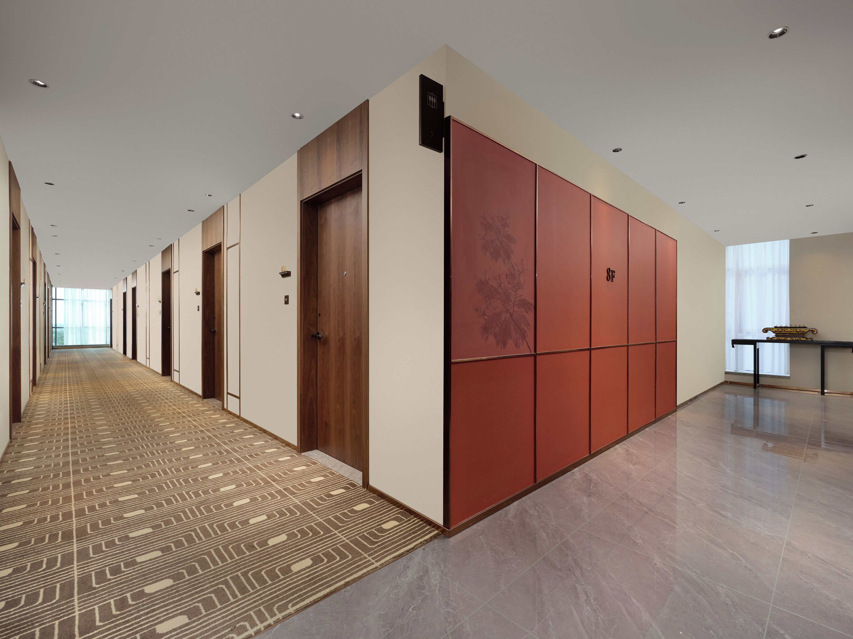 A long hallway with multiple doors, a patterned carpet, and a large window with sheer curtains.