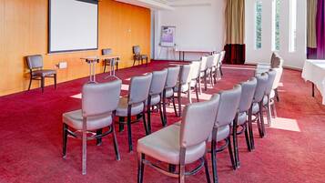 A conference room with rows of chairs, a projector screen, a whiteboard, and a large window with curtains.