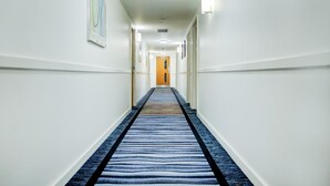 A hotel hallway with a striped carpet, white walls, and framed artwork.