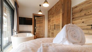 Un dormitorio con una cama grande, una bañera, un armario de madera y un televisor en la pared.