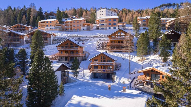 A snow-covered resort with multiple wooden buildings, including cabins and a larger hotel structure. - Inviting chalet on the ski-slope (Turracher Höhe)