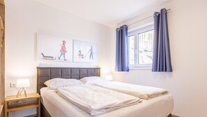 A bedroom with a double bed, a nightstand with a lamp, a window with curtains, and wall art depicting winter scenes. - Inviting chalet on the ski-slope (Turracher Höhe)