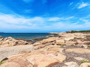 A rocky beach with clear blue sea and distant buildings.
