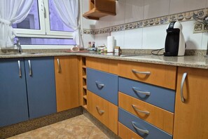 Eine Küche mit blauen und hölzernen Schränken, einer Arbeitsplatte, einer Kaffeemaschine und einem Fenster mit Vorhängen.