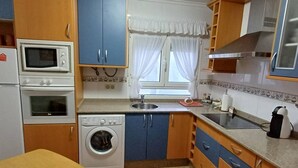 A compact kitchen with a washing machine, microwave, oven, and a sink. - 25A06 Centrico Playa 4 dormitorios Luanco (Luanco)