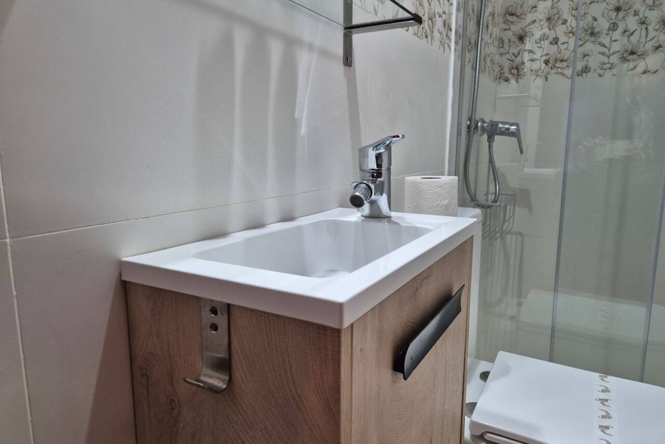 Ein Badezimmer mit einem weißen Waschbecken, einem Holzschrank und einer Duschkabine aus Glas.
