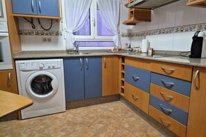 Una cocina con lavadora, armarios, un lavabo y una ventana con cortinas.