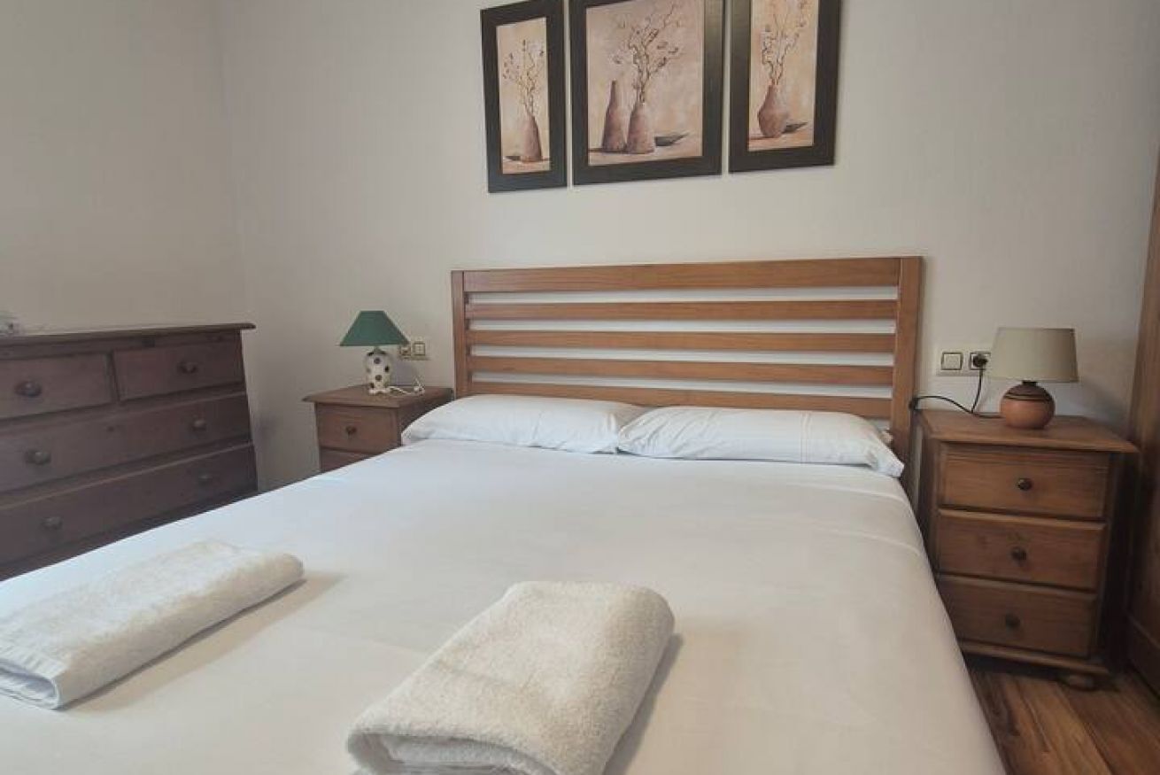 A neatly made bed with two towels, a wooden headboard, a nightstand with a lamp, and a dresser.