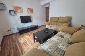 A living room with a sofa, a coffee table, a TV, and a wooden floor.