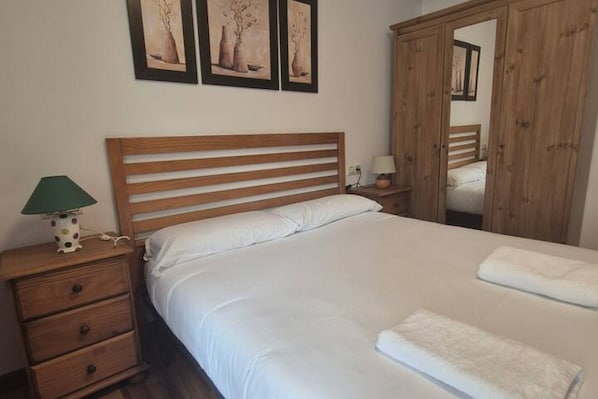 Un dormitorio con cama de madera, una mesita de noche con lámpara y un armario.
