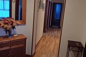 Un pasillo con piso de madera, un espejo en la pared y una pequeña mesa con un jarrón de flores secas.