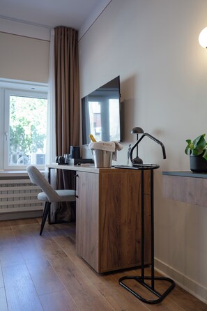 Een moderne hotelkamer met een houten bureau, een stoel, een flatscreen televisie aan de muur, een kleine zwarte lamp en een plantje op de vensterbank.