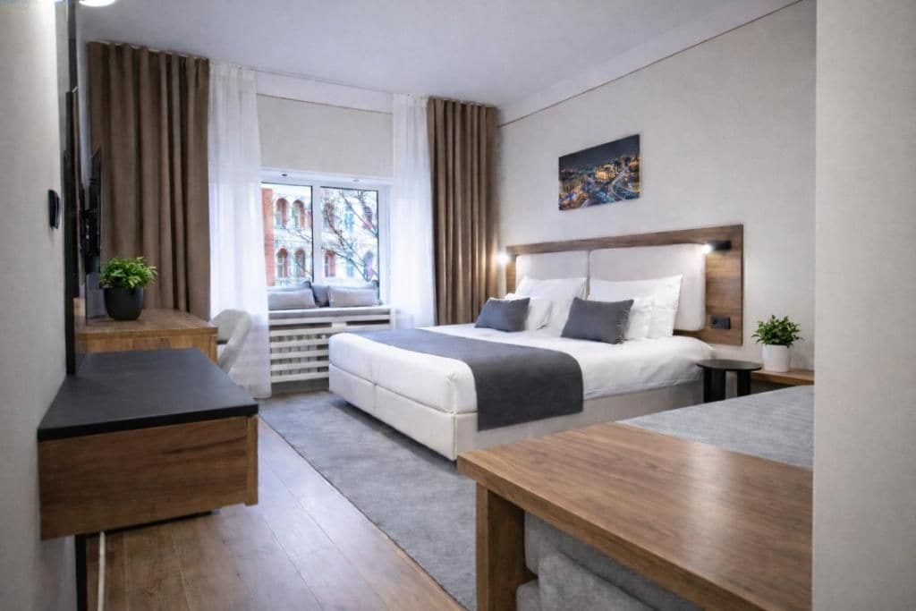 Una habitación de hotel moderna con cama, mesita de noche, escritorio y ventana con cortinas.