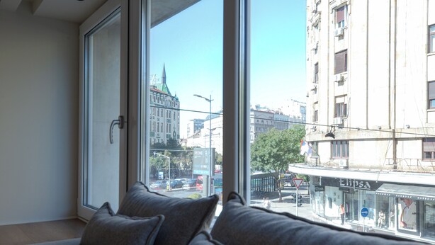 A room with a large window, a sofa, and a view of a cityscape. - Simma Luxury Apartments & Rooms (Belgrade)