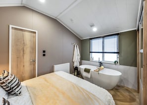 Une chambre avec un grand lit, une baignoire intégrée et une fenêtre équipée de stores.