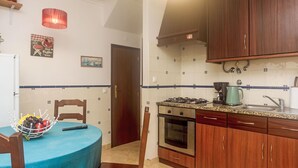 Eine Küche mit Holzausstattung, einem Gasherd, einem Backofen und einem Spülbecken. Ein Tisch ist mit einer blauen Tischdecke und einem Obstkorb bedeckt.