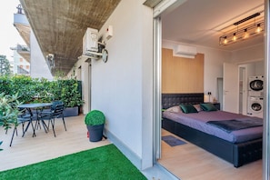 Un apartamento moderno con balcón, zona de comedor, dormitorio con cama y cabecera, y lavadora.