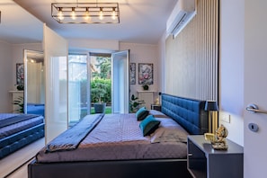 Un dormitorio con cama, mesitas de noche, espejo, radiador y vistas al exterior.