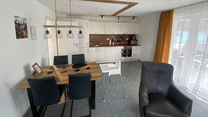 A modern kitchen with white cabinets, a wooden countertop, and a built-in oven. There is a dining area with a wooden table and black chairs.