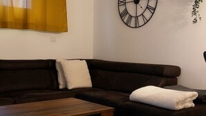 A dark brown sofa with a white throw blanket, a wooden coffee table, and a wall clock with Roman numerals.