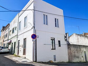 A white building with a no parking sign, a gas meter, and a narrow street.