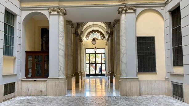 A spacious atrium with a tiled floor, large columns, and a central chandelier.