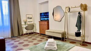 A hotel room with a bed, a desk, a chair, a vanity with a mirror, and a clothing rack.