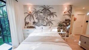 Ein Schlafzimmer mit einem großen Bett, einem Nachttisch, einem Spiegel und einer Wandmalerei von Palmen.