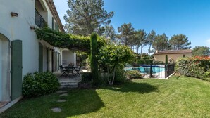 Um jardim bem cuidado com piscina, um alpendre com mobiliário exterior e um edifício com telhado em azulejos.