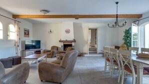 Uma sala de estar ampla com lareira, uma área de jantar com mesa e cadeiras, e uma televisão no canto.