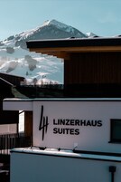 A building with a sign reading "Linzerhaus Suites" and a view of a snowy mountain in the background.