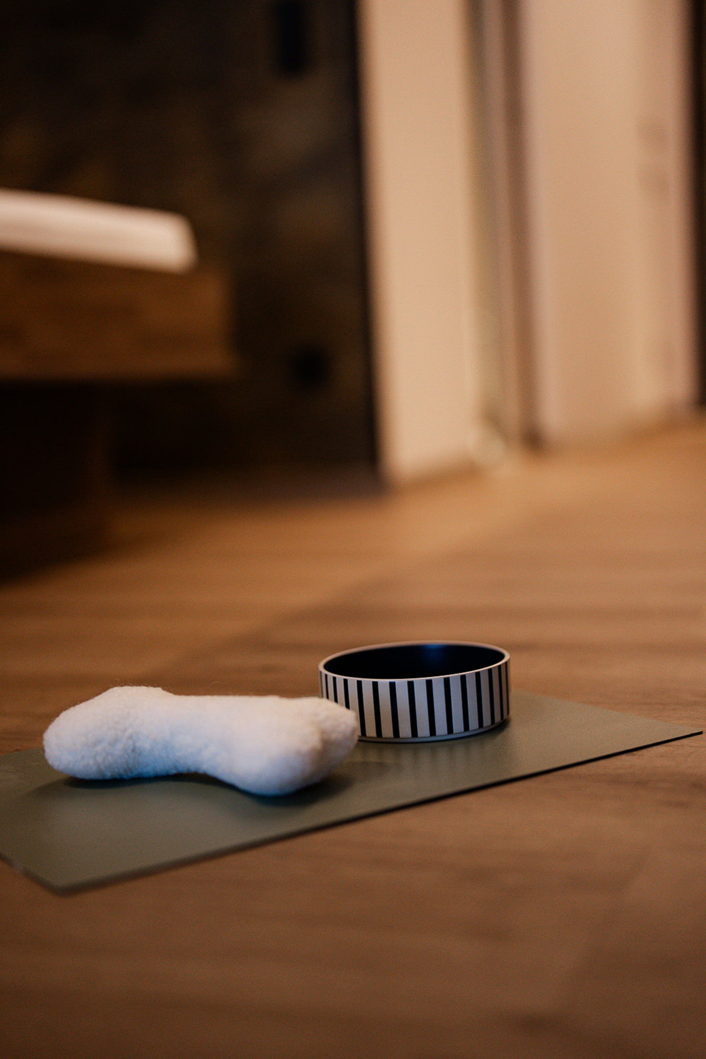 Un tapis de yoga, un rouleau de mousse blanc et une tasse à rayures, le tout posé sur un plancher en bois.