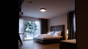 A modern hotel room with a large bed, a small sofa, and a balcony with a view of trees. - LH Linzerhaus Suites Saalbach – inklusive Jokercard (Saalbach-Hinterglemm)