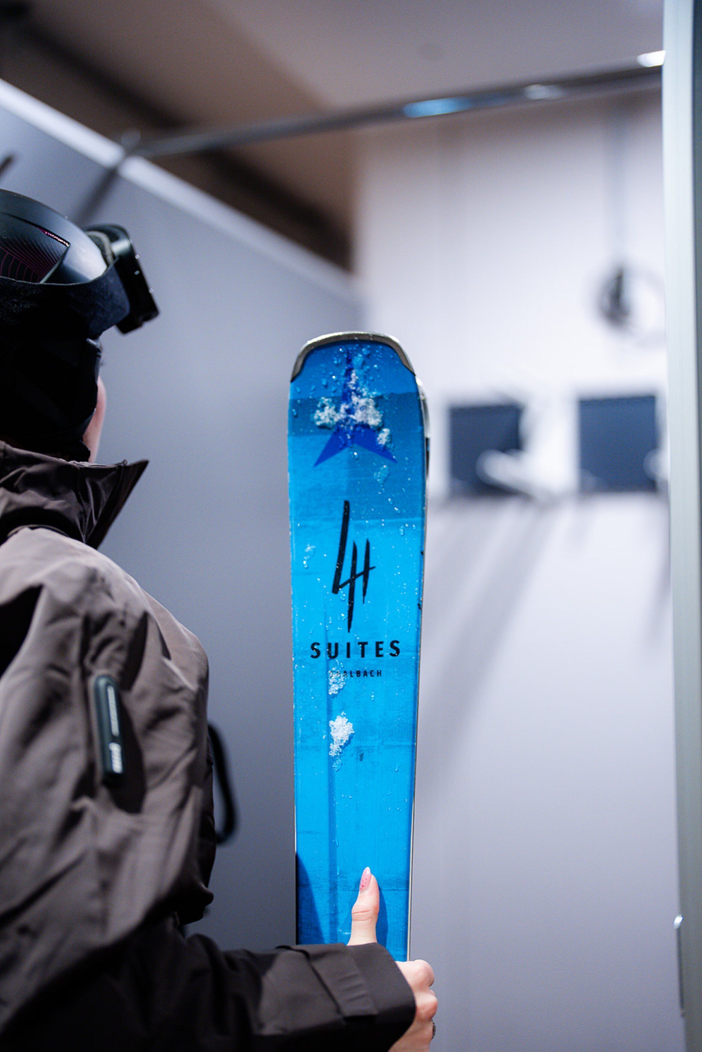 Une personne tenant une planche de snowboard bleue sur laquelle on peut lire les mots « 4 SUITES » et « SUIETES ».