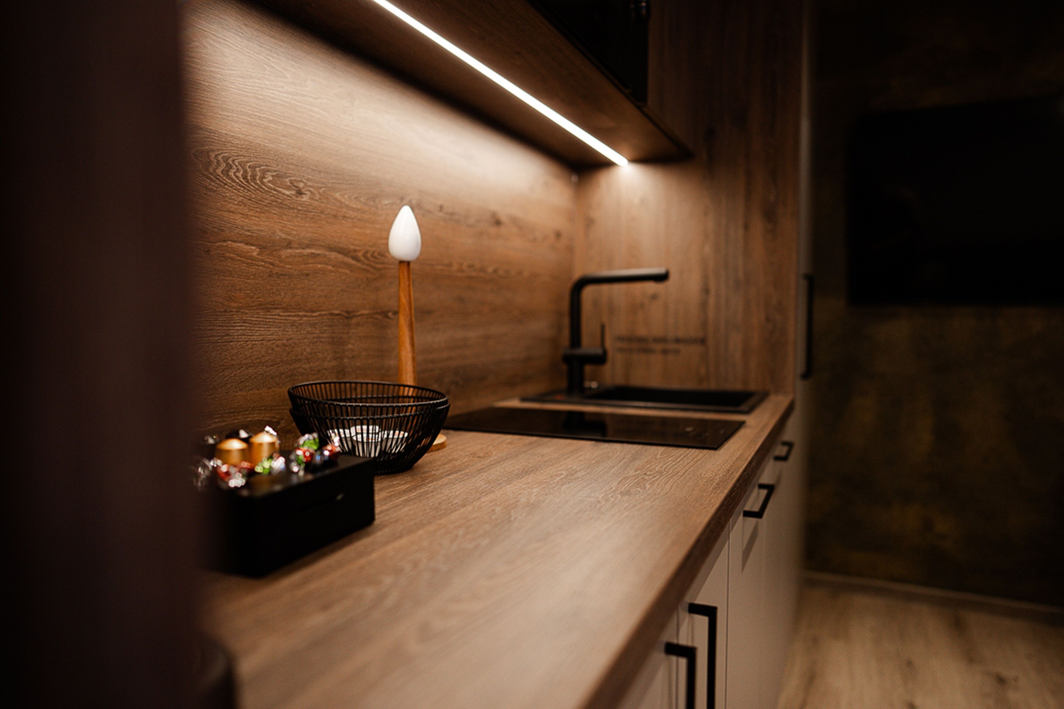 A modern kitchen with wooden cabinetry, a black sink, and a countertop with a black basket containing decorative items.