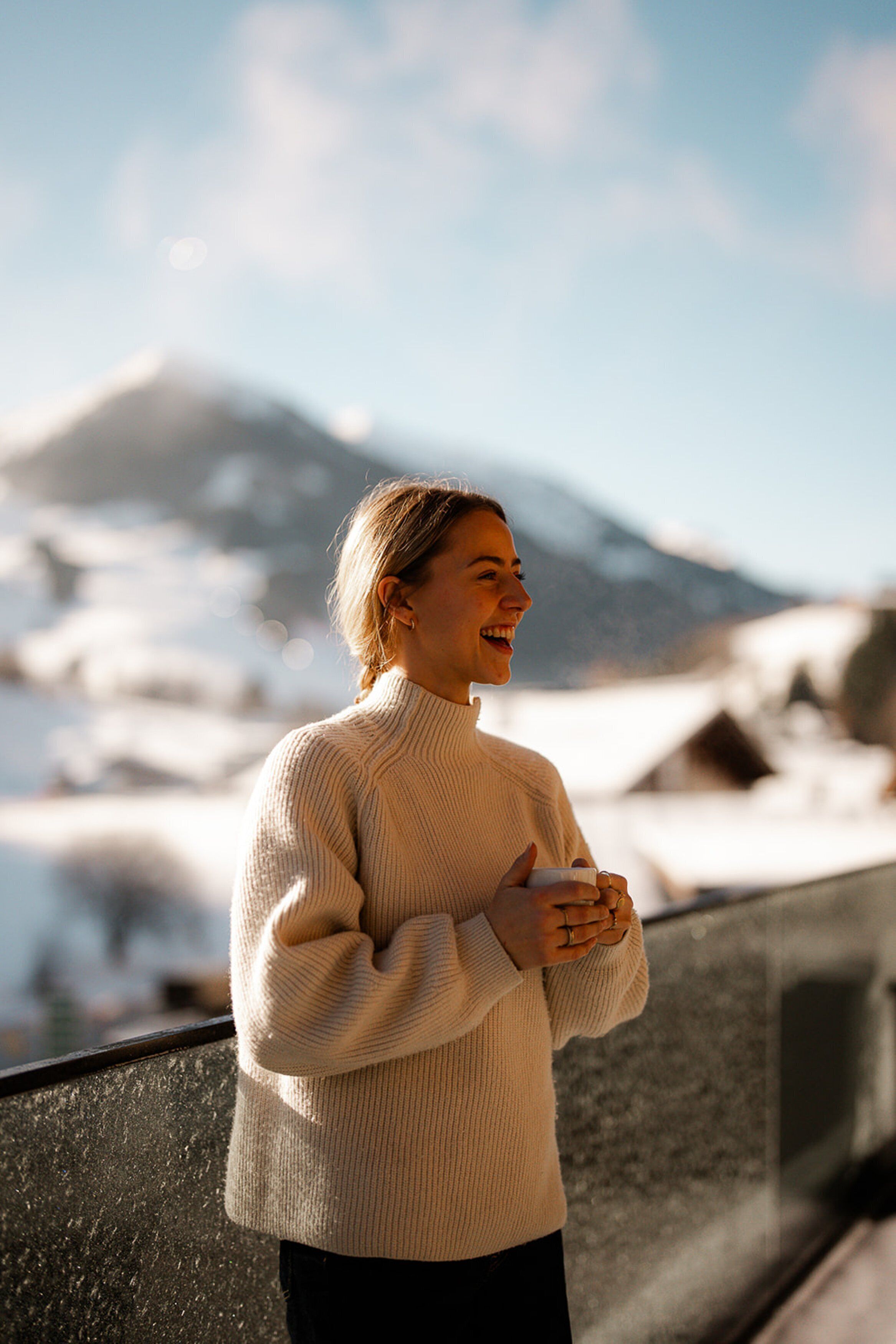 A person standing by a window overlooking a snowy landscape with mountains in the background.
