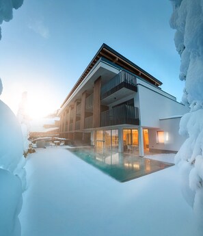 A modern building with a glass pool, surrounded by snow. - LH Linzerhaus Suites Saalbach (Saalbach-Hinterglemm)