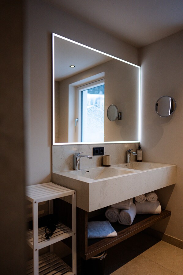 A modern bathroom with a large mirror, two sinks, and a towel rack. - LH Linzerhaus Suites Saalbach (Saalbach-Hinterglemm)