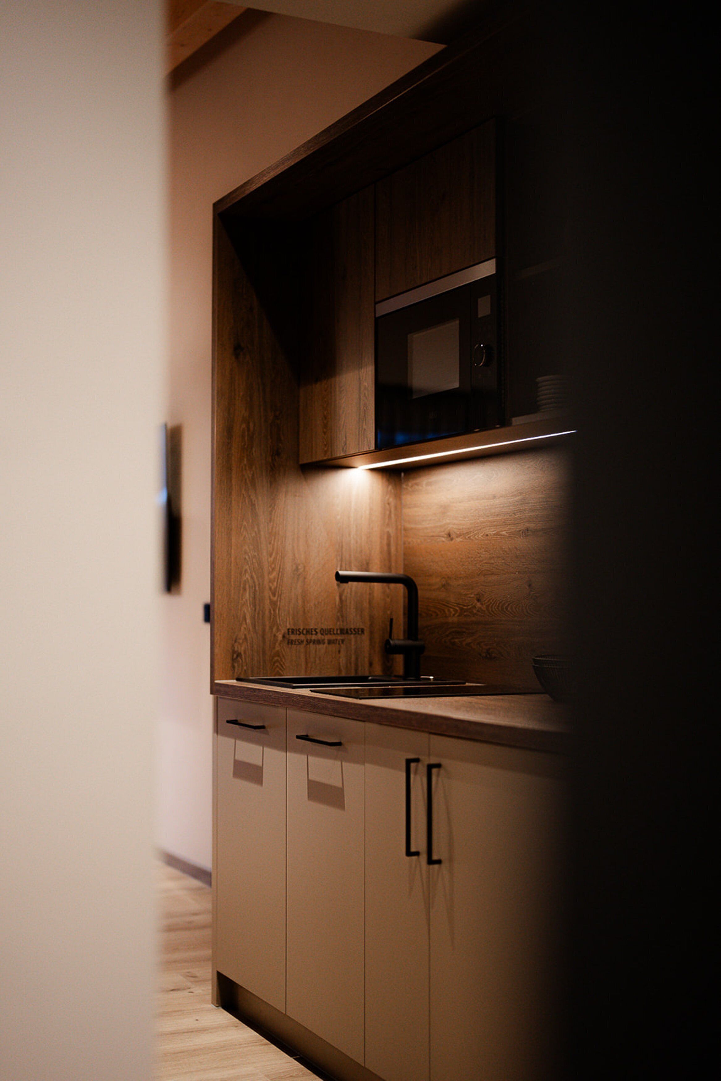 Una cocina moderna con armarios de madera, un lavamanos de acero inoxidable y un microondas.
