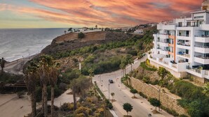 A coastal view with a sunset, a road, and a modern building with balconies.
