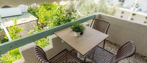Un balcón con una mesa, dos sillas, una planta en maceta y vistas a zonas verdes y edificios.