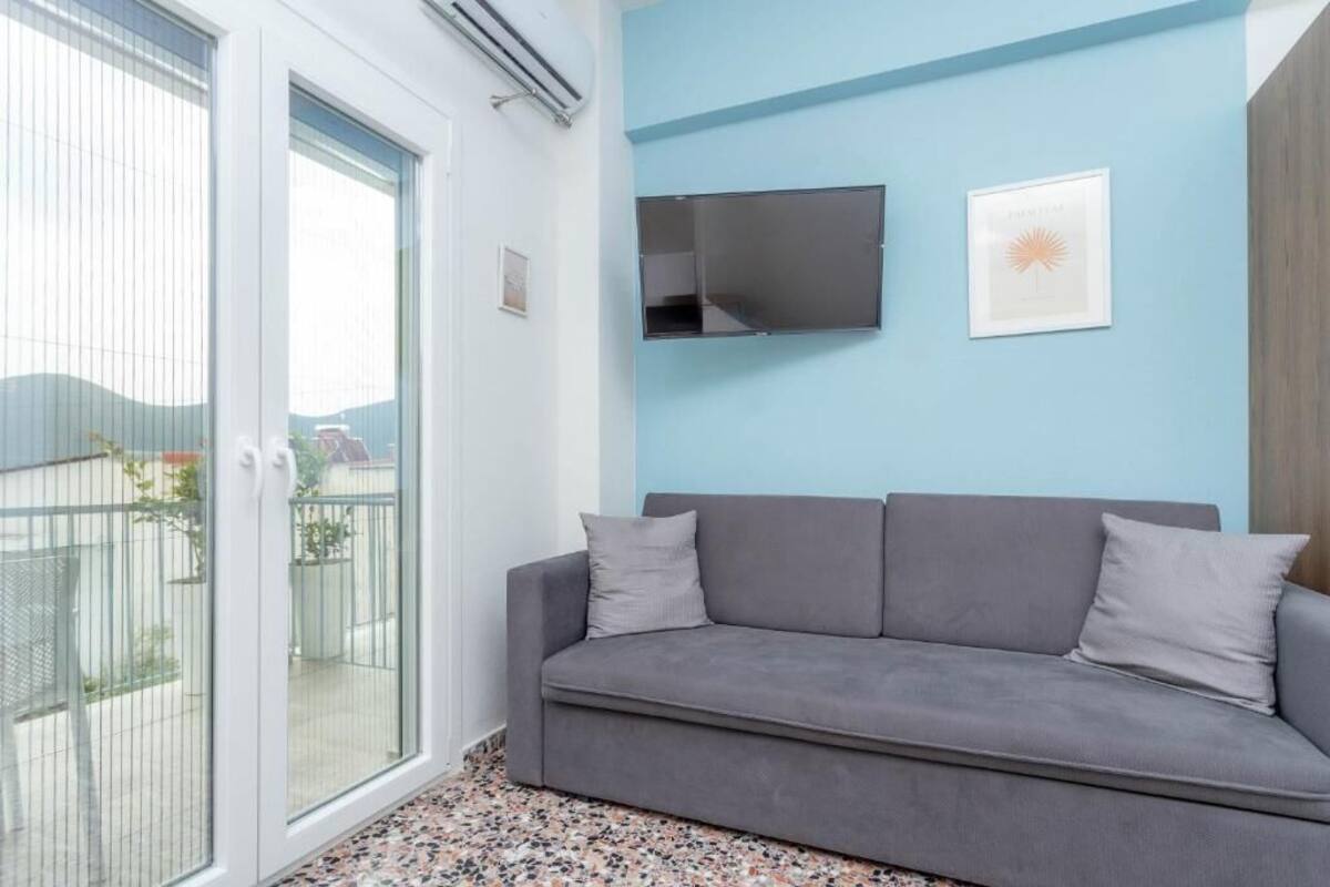 A modern living room with a grey sofa, a mounted TV, and a framed artwork on a light blue wall.