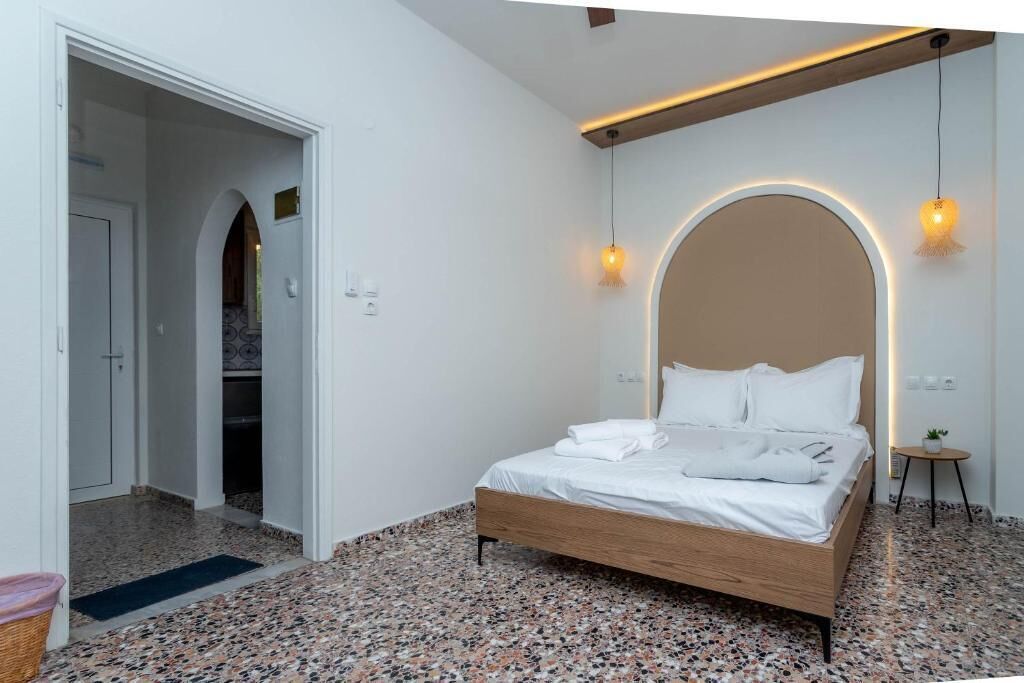A bedroom with a bed, a door, a small table with a plant, and a wall with a light fixture.