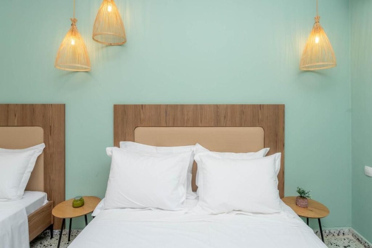 A hotel room with two beds, a wooden headboard, a small round table with a candle, and three hanging lamps.