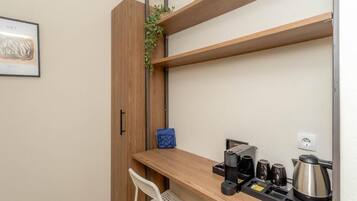 Een kleine kitchenette met een koffiezetapparaat, kopjes en een waterkoker op een houten aanrecht.